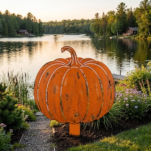 May include: A flat, orange metal pumpkin garden stake with a cutout design featuring vertical segments and a curved stem. The pumpkin is mounted on a rectangular metal post, designed to be inserted into the ground for outdoor decoration.