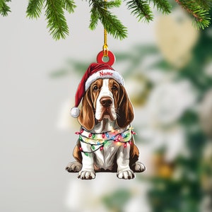 May include: A Christmas ornament featuring a cartoon Basset Hound wearing a Santa hat and a string of colorful lights. The ornament has a red and white Santa hat with the word "Name" written on it.