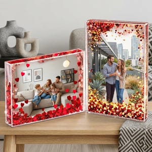 May include: Two rectangular clear acrylic photo frames filled with liquid and floating red heart-shaped glitter. One frame is horizontal, displaying a family on a sofa, and the other is vertical, showing a couple standing outdoors.