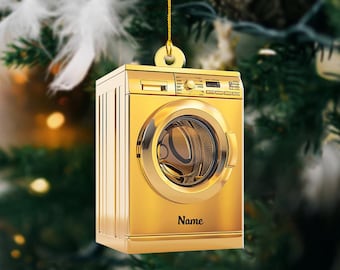 Könnte beinhalten: Ein goldfarbener Waschmaschinen-Anhänger mit einem Namensschild, auf dem "Name" steht. Der Anhänger hängt an einer goldenen Schnur an einem Weihnachtsbaum.