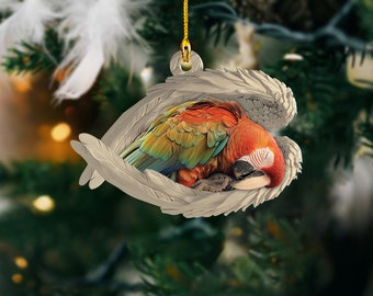 Könnte beinhalten: Ein Weihnachtsbaumschmuck mit einem bunten Ara-Papagei mit roten, gelben, grünen und blauen Federn, der in einem weißen, geformten Engelsflügel-Anhänger schläft.