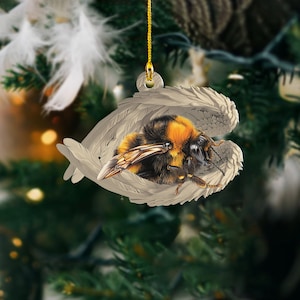 May include: A Christmas ornament featuring a bumblebee with black and yellow stripes resting inside a pair of white wings.