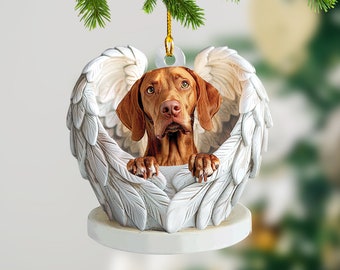 Könnte beinhalten: Ein brauner und weißer Hund mit Engelsflügeln als Ornament. Der Hund schaut mit traurigem Ausdruck in die Kamera. Das Ornament ist aus weißer Keramik und hat eine goldene Schnur.