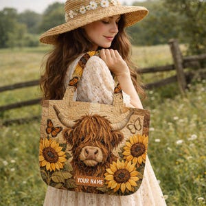May include: A quilted tote bag featuring a central Highland cow illustration surrounded by yellow sunflowers and orange butterflies. The bag has a rectangular shape with two shoulder straps and a rectangular patch at the bottom with the text YOUR NAME.