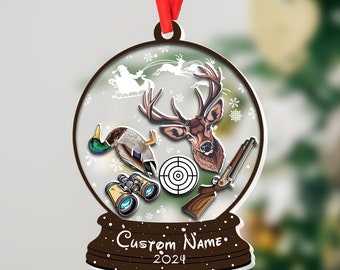 Könnte beinhalten: Runder Weihnachtsschmuck mit Jagdmotiv. Der Schmuck zeigt einen Hirschkopf, eine Ente, ein Fernglas, ein Gewehr und eine Zielscheibe. Der Text "Custom Name" und "2024" sind ebenfalls enthalten. Ein rotes Band ist zum Aufhängen befestigt.
