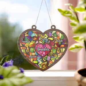 May include: A wooden heart-shaped ornament with a stained glass design. The heart is divided into puzzle pieces, each with a name: Sophia, Luna, Noah, David, Mia, and Grandma.