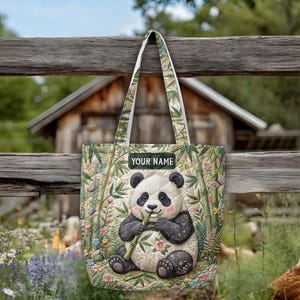 May include: A quilted tote bag featuring a central illustration of a panda eating bamboo stalks. The design includes a background of green bamboo leaves, small pink flowers, and butterflies. A rectangular label at the top reads YOUR NAME.