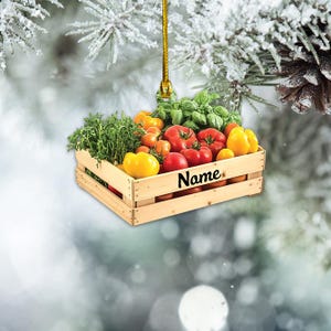 May include: A wooden crate filled with red and yellow tomatoes, green leafy vegetables, and a basil sprig. The crate is hanging from a string and has the word "Name" written on it.