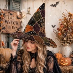 May include: A pointed witch hat featuring a patchwork design of velvet and textured fabrics in shades of black, dark green, purple, and burnt orange, accented with gold embroidered celestial motifs and decorative cross-stitching throughout.