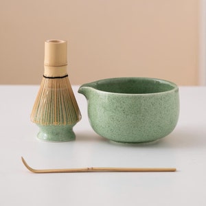 May include: A green ceramic matcha bowl with a bamboo whisk and a bamboo matcha scoop. The bowl has a speckled green glaze.