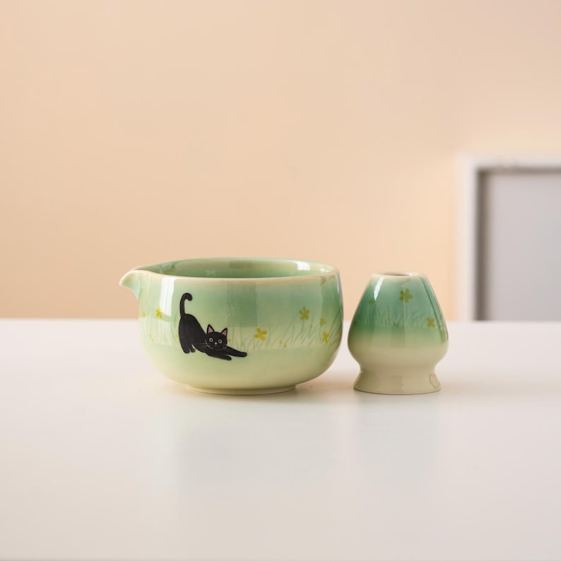 Pu&ograve; includere: Una tazza da t&egrave; in ceramica verde con un design di gatto nero e un coperchio in ceramica verde abbinato.