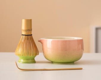 Può includere: Una ciotola di matcha in ceramica rosa e verde con una frusta di bambù e un cucchiaio di matcha in legno.