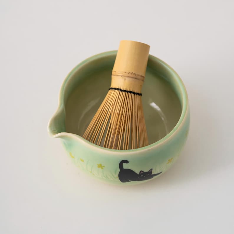 Pu&ograve; includere: Una ciotola di matcha in ceramica verde con un design di gatto nero e uno sbattitore di bamb&ugrave; all'interno.