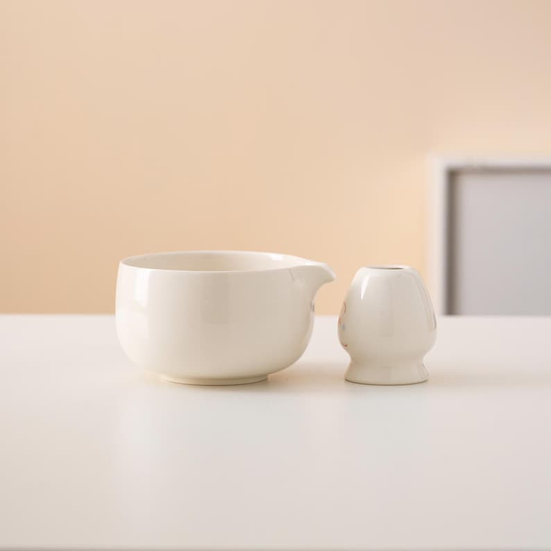 Pu&ograve; includere: Un'anfora in ceramica bianca e un piccolo vaso in ceramica bianca su una superficie bianca.