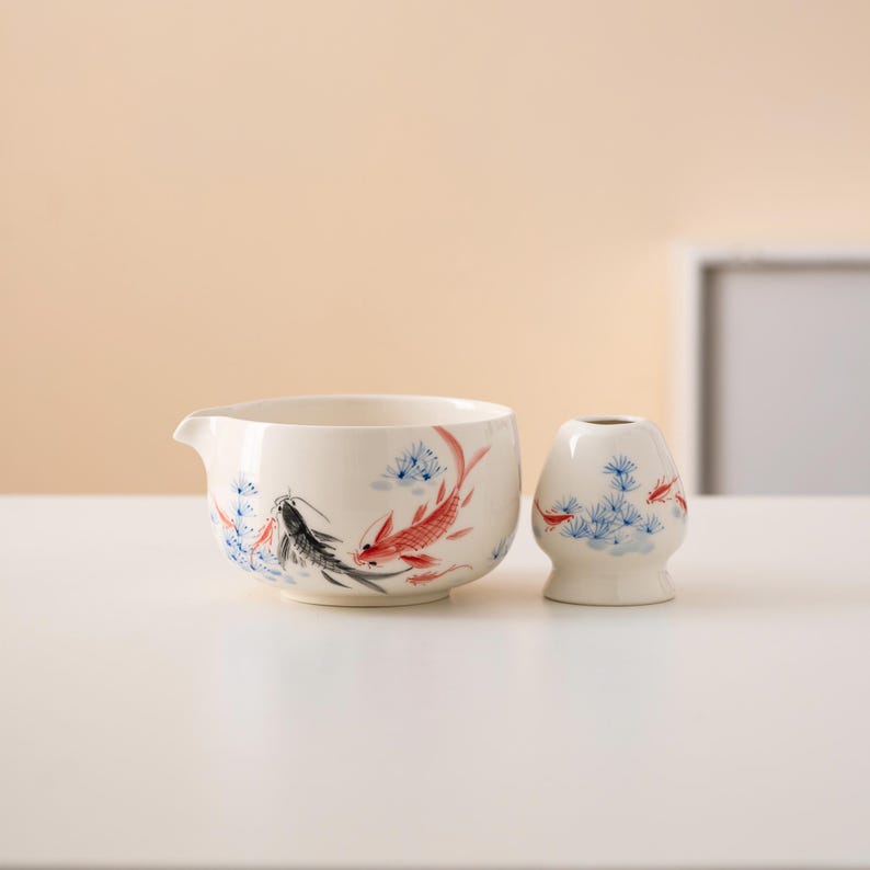 Pu&ograve; includere: Un set da t&egrave; in ceramica bianca con un design di pesci blu e rossi. Il set comprende un'ampolla e una piccola tazza.