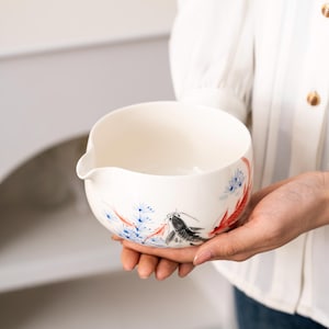 Pu&ograve; includere: Scodella in ceramica bianca con un design floreale blu e rosso e un design di pesce nero e rosso. La ciotola ha un beccuccio su un lato.