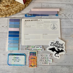 May include: A collection of book-themed items, including books, highlighters, sticky notes, stickers, and a book review notepad. The stickers have phrases like "Book Dragon" and "You had me at trigger warnings."