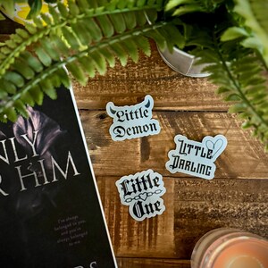 May include: Three white stickers with black gothic lettering. The stickers say "Little Demon", "Little Darling", and "Little One" with a heart and chain design.