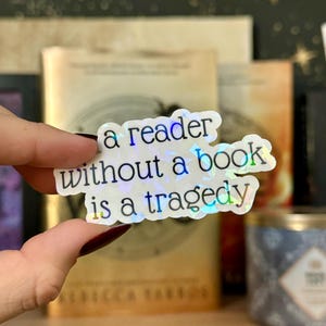 Op de afbeelding: Een holografische sticker met de tekst "a reader without a book is a tragedy".