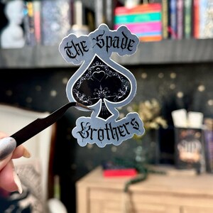 May include: A silver sticker with a black spade design and the text "The Spade Brothers".