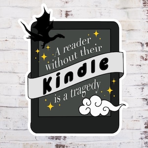 May include: A black and white sticker with a black dragon, a cloud, and stars. The sticker says "A reader without their Kindle is a tragedy."