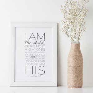 May include: Black and white typography print with a white frame. The print features a quote from the Bible, 2 Corinthians 6:18, which reads "I am the child of the most high king who is not moved by the world for my God is with me and goes before me I do not fear because I am his."