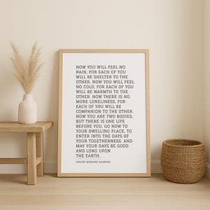 May include: A framed print with the text of the Apache Wedding Blessing in black font. The print is in a light wood frame and is displayed on a wall. A small wooden table with a white vase and dried flowers is to the left, and a woven basket is to the right.