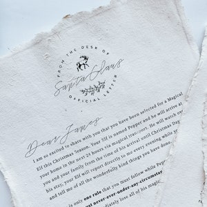 May include: Off-white paper with torn edges, featuring a handwritten letter from Santa Claus. The text includes "FROM THE DESK OF SANTA CLAUS OFFICIAL LETTER" and a message to "Dear James" about an elf named Pepper.