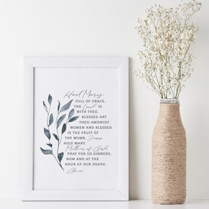 May include: A framed print with a blue watercolor floral design and the text "Hail Mary, full of grace, the Lord is with thee. Blessed art thou amongst women and blessed is the fruit of thy womb, Holy Mary, Jesus, Mother of God. Pray for us sinners, now and at the hour of our death. Amen."