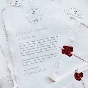 May include: A stack of textured white paper with handwritten text, featuring a circular logo that reads "From the Desk of Santa Claus." The letters are sealed with red wax stamps and tied with twine. The theme is a letter from Santa.