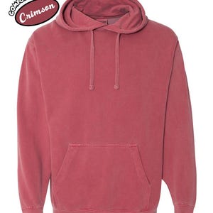 以下が含まれることがあります： ドローストリングフードとフロントカンガルーポケットが付いたクリムゾンカラーのパーカー。「Comfort Colors」と「Crimson」の文字が左上にプリントされています。