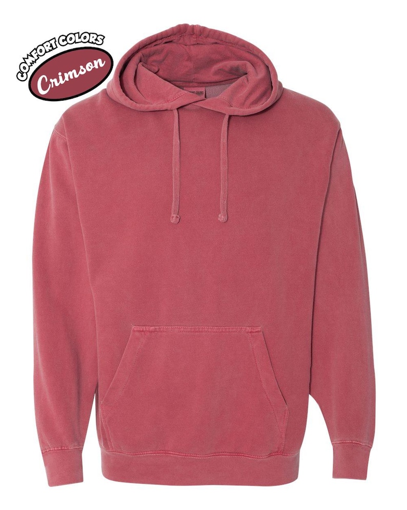 以下が含まれることがあります： ドローストリングフードとフロントカンガルーポケットが付いたクリムゾンカラーのパーカー。「Comfort Colors」と「Crimson」の文字が左上にプリントされています。
