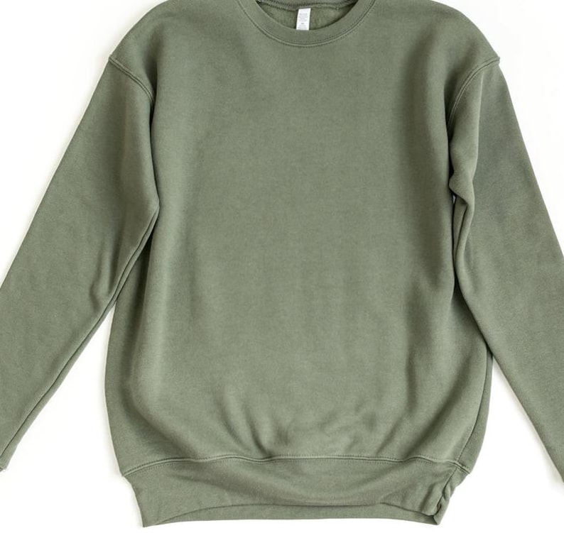 May include: A solid olive green crewneck sweatshirt. The long-sleeved top has a ribbed hem and cuffs, and a crew neckline. The sweatshirt is made of a soft, comfortable material.