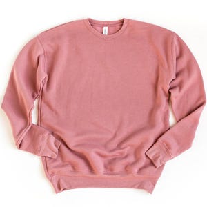 May include: A solid mauve-colored sweatshirt with a crew neck and long sleeves. The cuffs and hem are ribbed. The tag is visible at the back of the neck. The sweatshirt is made of a soft material.