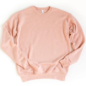 May include: A solid-colored, long-sleeved sweatshirt in a soft, muted pink hue. The crew neck sweatshirt has ribbed cuffs and hem. The fabric appears to be a soft, comfortable material. A simple, casual top for everyday wear.