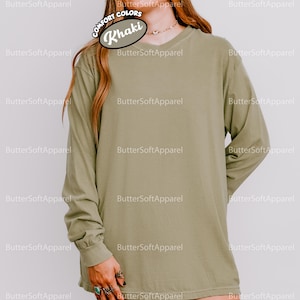 May include: Khaki long-sleeved shirt with a V-neck. The shirt is a solid colour and has a relaxed fit. The text "COMFORT COLORS" and "Khaki" are visible on the top left of the shirt. The brand name "ButterSoftApparel" is printed around the shirt.