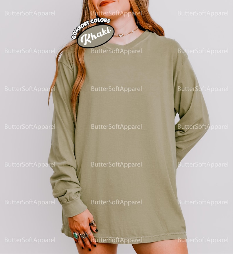 May include: Khaki long-sleeved shirt with a V-neck. The shirt is a solid colour and has a relaxed fit. The text "COMFORT COLORS" and "Khaki" are visible on the top left of the shirt. The brand name "ButterSoftApparel" is printed around the shirt.