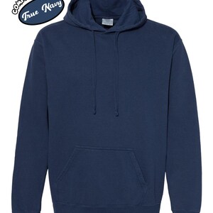 以下が含まれることがあります： フロントポケットとドローストリングフードが付いたネイビーブルーのパーカー。パーカーの左上に白い楕円で「Comfort Colors True Navy」の文字が入っています。この衣服は柔らかく快適な素材で作られています。