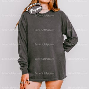 May include: A dark grey long-sleeved shirt with a crew neck. The shirt is made of a soft, comfortable material. The shirt has the text "Pepper" on the upper left side. The shirt is part of the Comfort Colors collection.