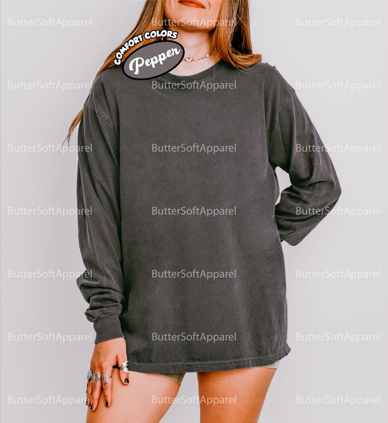 May include: A dark grey long-sleeved shirt with a crew neck. The shirt is made of a soft, comfortable material. The shirt has the text "Pepper" on the upper left side. The shirt is part of the Comfort Colors collection.