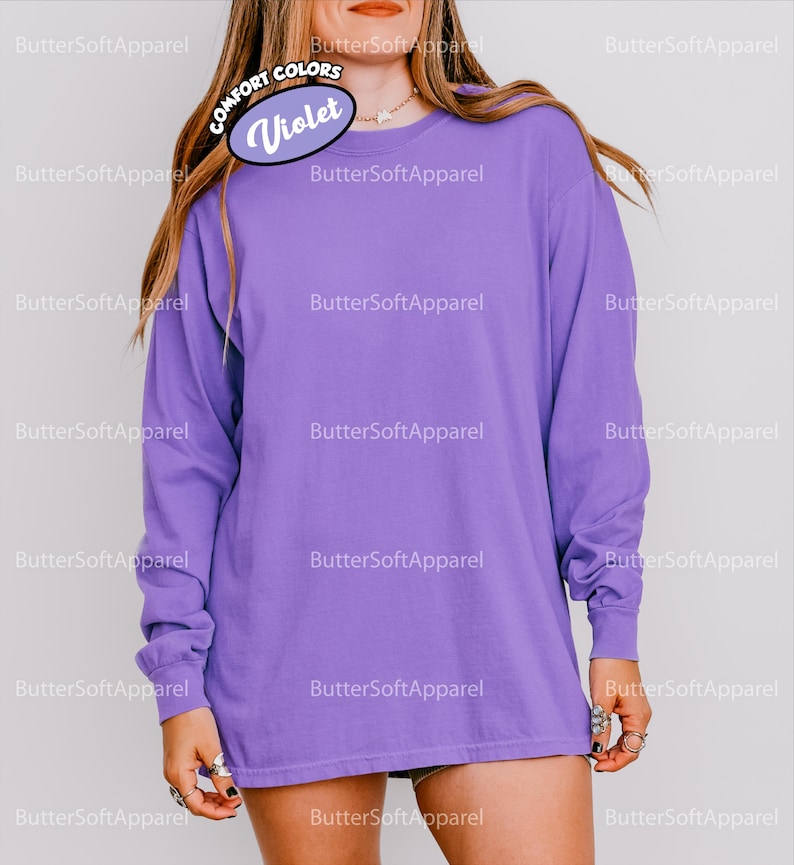 May include: A long-sleeved violet shirt. The shirt has a crew neck and is a solid colour. The image includes the text "COMFORT COLORS" and "Violet". The brand name "ButterSoftApparel" is also visible.