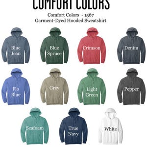 以下が含まれることがあります： Comfort Colorsのガーメントダイ加工フーディーのスウェットシャツのディスプレイ。Blue Jean、Blue Spruce、Crimson、Denim、Flo Blue、Grey、Light Green、Pepper、Seafoam、True Navy、Whiteなど様々な色があります。ブランド名とスタイルが上部に表示されています。