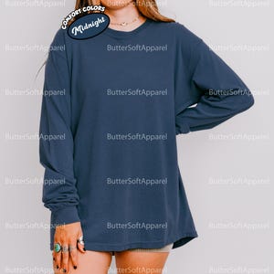 May include: A navy blue long-sleeved shirt with a crew neck and a relaxed fit. The text "Midnight" is displayed on a circular label. The shirt is made of a soft, comfortable material. Part of the Comfort Colors collection.