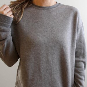 May include: A heather gray sweatshirt with a crew neck and long sleeves. The casual top is made of a soft material and has a relaxed fit. The sweatshirt is a solid color and suitable for everyday wear.