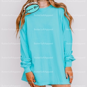 May include: A turquoise long-sleeved t-shirt. The shirt is a solid colour and has the text "COMFORT COLORS" and "Lagoon Blue" on a tag. The shirt is a relaxed fit and has long sleeves. The shirt is made of a soft material.