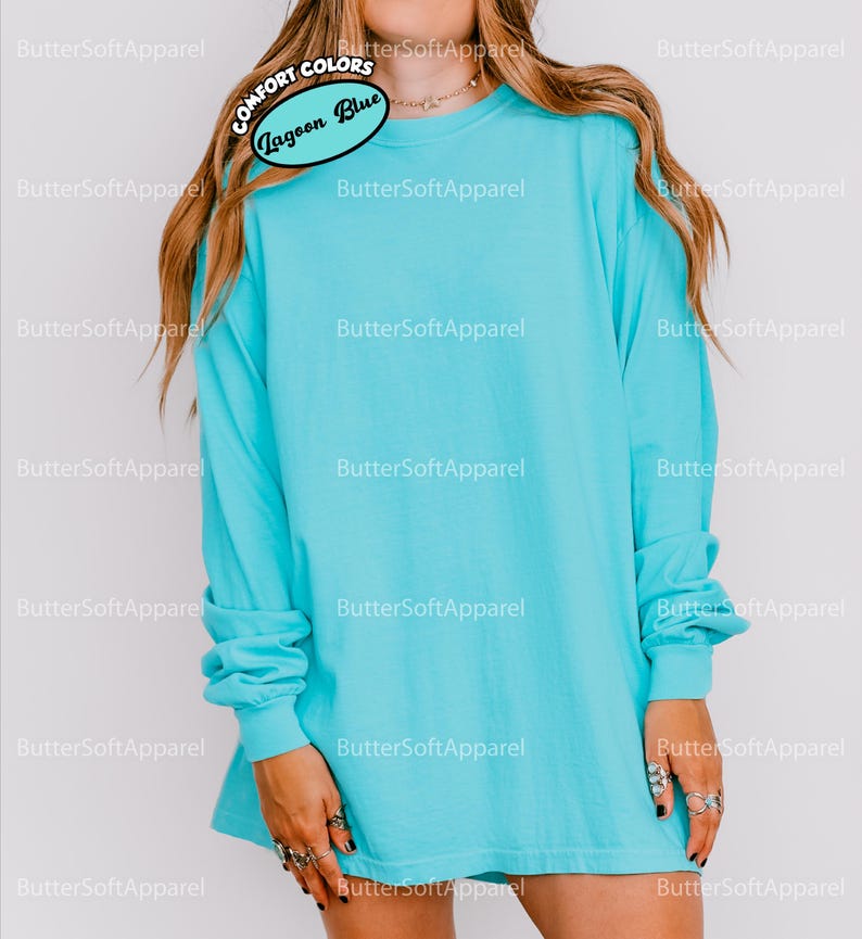 May include: A turquoise long-sleeved t-shirt. The shirt is a solid colour and has the text "COMFORT COLORS" and "Lagoon Blue" on a tag. The shirt is a relaxed fit and has long sleeves. The shirt is made of a soft material.
