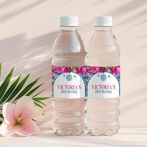 May include: Two clear water bottles with white caps. Each bottle has a label with the text "Victoria's 28th Birthday" in pink and blue. Pink flowers and green leaves are in the background.