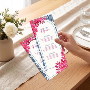 Może przedstawiać: Dwie karty menu z kwiatowymi i niebieskimi wzorami. Karty menu mają tytuł "The Menu" w kursywie. Karty są ozdobione różowymi kwiatami. Po lewej stronie wazon z białymi różami i zielenią.