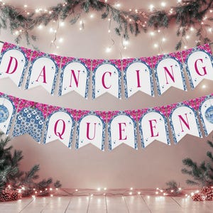 May include: A banner with the words "DANCING QUEEN" in burgundy letters. The banner has a white background with a blue and pink floral design. A disco ball is on each end of the banner. The banner is strung between two evergreen trees.