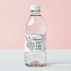 Puede incluir: Una botella de agua de plástico transparente con tapa blanca. La etiqueta presenta una mano de esqueleto haciendo el signo de la paz y el texto "Sabrina's BAD TWO the BONE" en escritura negra. La etiqueta tiene un patrón de cuadros rosas y blancos.